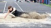 Athlete landing in a long jump sand pit at an outdoor track and field event.