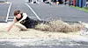 Athlete landing in a long jump sand pit at an outdoor track and field event.