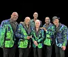 Five men stand together in matching green and blue sequined jackets against a black background.