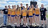 A large group of athletes and coaches stands together outdoors in matching yellow uniforms.