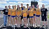 A large group of athletes and coaches stands together outdoors in matching yellow uniforms.