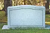 A blank granite memorial marker on a lawn with trees behind it.