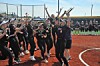 Softball players in black uniforms cheer together on a dirt field near home plate.