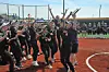 Softball players in black uniforms cheer together on a dirt field near home plate.