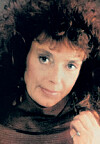 Close-up portrait of a woman in a dark fur-trimmed coat, looking at the camera.