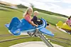 Children sit on a blue spinning playground ride at an outdoor amusement area.