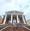 Brick building with white columns, flags, and a staircase viewed from below.