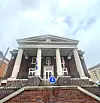 Brick building with white columns, flags, and a staircase viewed from below.