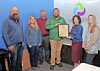 A group stands indoors while one person holds a framed certificate during an award presentation.