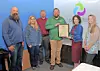 A group stands indoors while one person holds a framed certificate during an award presentation.