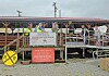 People gathered on a raised rail platform with signs and a railroad crossing marker in front.