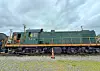 Green and yellow locomotive parked on railroad tracks with an orange cone in front.