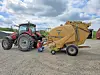 Red tractor and yellow farm equipment in a gravel yard with a person kneeling beside the machinery.