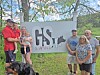 A small group stands beside a GS Swine sign outdoors near trees and grass.