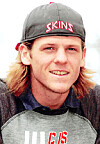 Close-up of a young man wearing a gray cap with “SKINS” on the front.