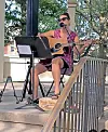 Musician seated on an outdoor stage plays guitar and sings into a microphone during Arts Week 2026.