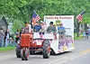 A red tractor pulls a decorated parade float past spectators on a neighborhood street.