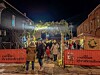 People walking under lights and greenery at the Mohican Christkindlmarkt entrance at night.