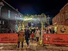People walking under lights and greenery at the Mohican Christkindlmarkt entrance at night.