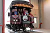 Several people ride on an open-air vintage railcar decorated with bunting inside a large indoor facility.