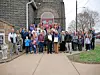 A large group poses outside a stone church building with an arched entrance.