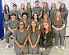 A group of students in gray scrubs poses for a photo indoors.