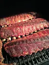 Three slabs of ribs cooking on a grill with darkened, charred surfaces.