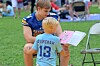 Two boys in football jerseys look at an open booklet on a grassy field beside a folding chair.