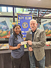 A student and a man hold a check in front of a Key Club banner and yearbook table display.