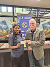 A student and a man hold a check in front of a Key Club banner and yearbook table display.