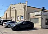 Beige brick commercial building with a sign, glass block windows, and parked cars in front.