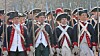 Group of men in historical military uniforms and tricorn hats standing in a line outdoors.