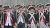 Group of men in historical military uniforms and tricorn hats standing in a line outdoors.