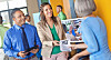 People stand around a table with display materials during an indoor presentation.