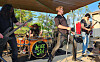 A rock band plays on an outdoor stage with drums, guitars, and microphones.