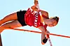 A pole vaulter in a red uniform arching over the bar during an outdoor competition.