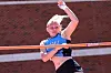 Young athlete in blue clears a hurdle outdoors in front of a brick building.