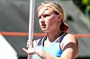 A pole vaulter wearing a blue uniform holds a pole and looks ahead during an outdoor event.