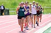 Several runners race along a pink track with green grass beside it.