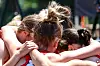 Several athletes lean in with arms around each other in a tight huddle outdoors.