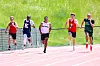 Five runners compete on a track with green grass behind them.