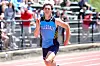 Runner in a blue Hillsdale uniform sprinting on a track with spectators behind him.