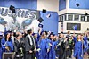 Graduates in blue gowns toss caps in the air during a commencement ceremony indoors.