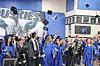 Graduates in blue gowns toss caps in the air during a commencement ceremony indoors.