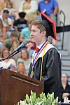 Graduate in cap and gown speaking at a podium during a commencement ceremony.