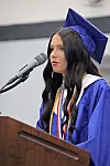 Graduate in blue cap and gown speaking at a podium with a microphone.