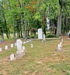 Small cemetery with old gravestones and memorial markers beneath trees in fall colors.