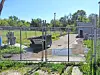 A chain-link fenced utility area with metal equipment and concrete pads next to a paved path and grass.