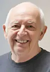 Close-up portrait of a smiling older man against a neutral background.