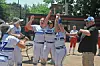 Softball players in blue and gray uniforms celebrate near a bench while someone takes a photo.